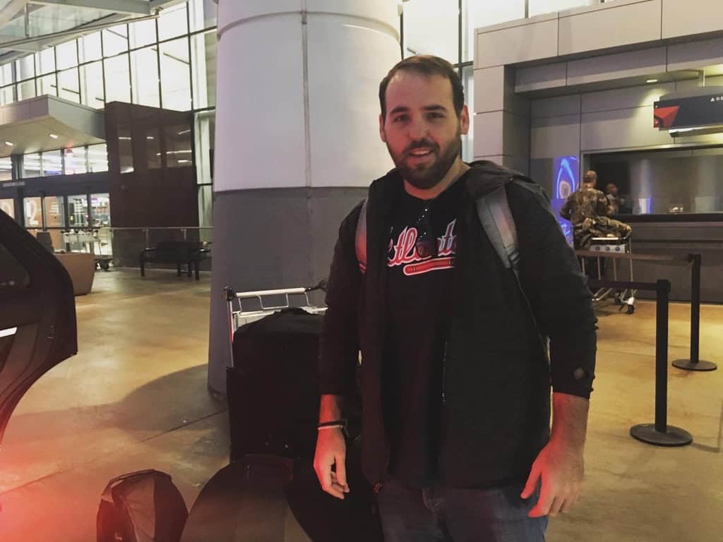 Chaz Chambers stands beside luggage at an airport check-in area, wearing a backpack.