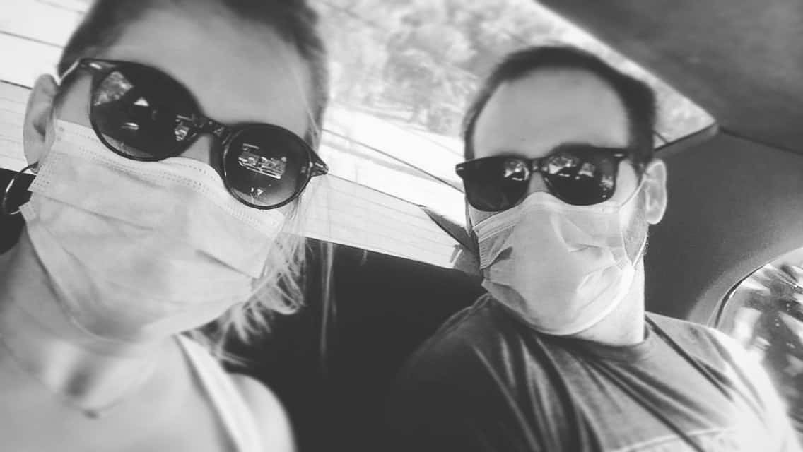 Black-and-white selfie of Yami and Chaz wearing face masks and sunglasses in the back seat of a car.
